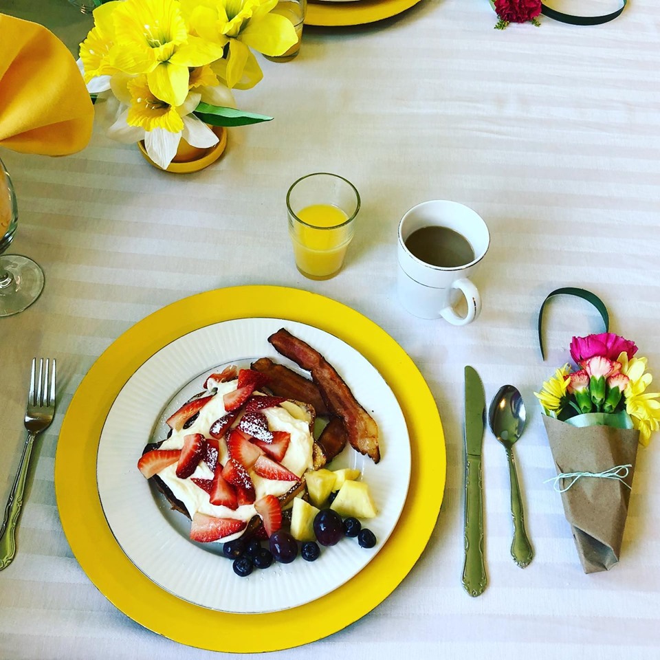 Mothers Day breakfast table setting, orange juice, lemon cream french toast, berries, bacon, and a bouquet of flowers